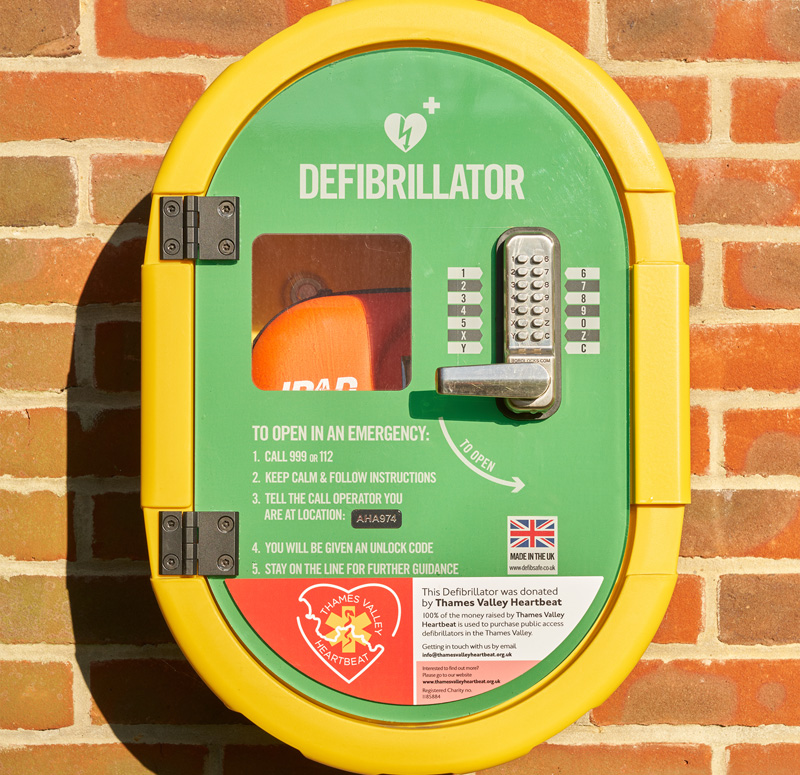 A defibrillator in its protective case, mounted on red brick wall