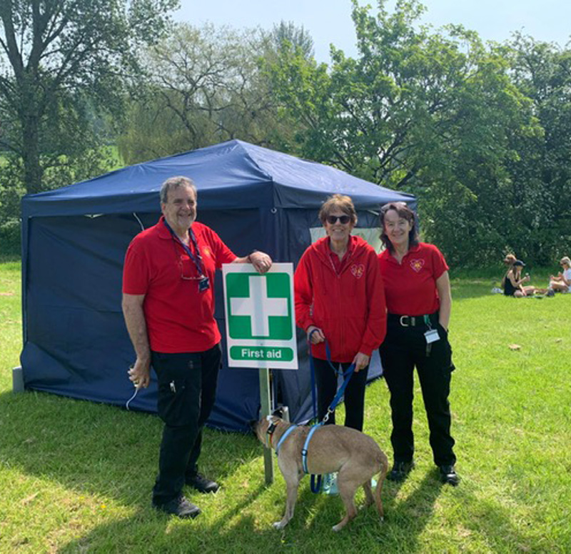 Some of our first aiders at an event, standing in a field in front of a blue first aid gazebo